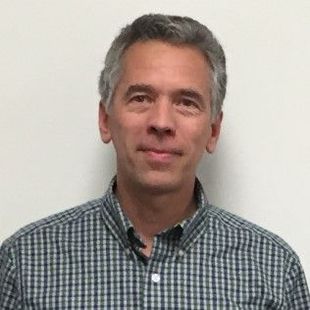 Man with graying hair wearing a blue and gray plaid shirt.