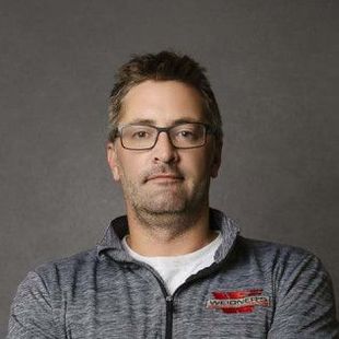 Man wearing glasses and a gray zip-up sweatshirt, against a gray backdrop.