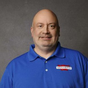 Man with bald head and blue polo shirt, smiling at camera. Logo on shirt.