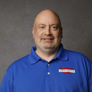 Man with bald head and blue polo shirt, smiling at camera. Logo on shirt.
