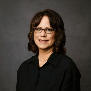 Woman wearing glasses and a black shirt smiling at the camera. Dark background.