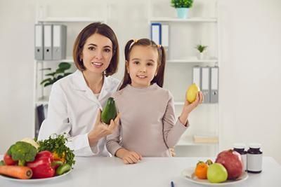 A nutritionist and child holding produce, smiling at the camera in an office.
