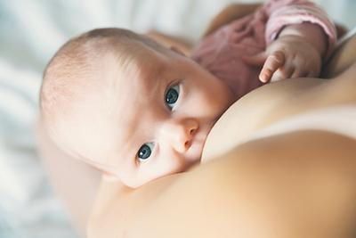 Baby with blue eyes nursing, looking at the camera. Pink shirt, soft focus.