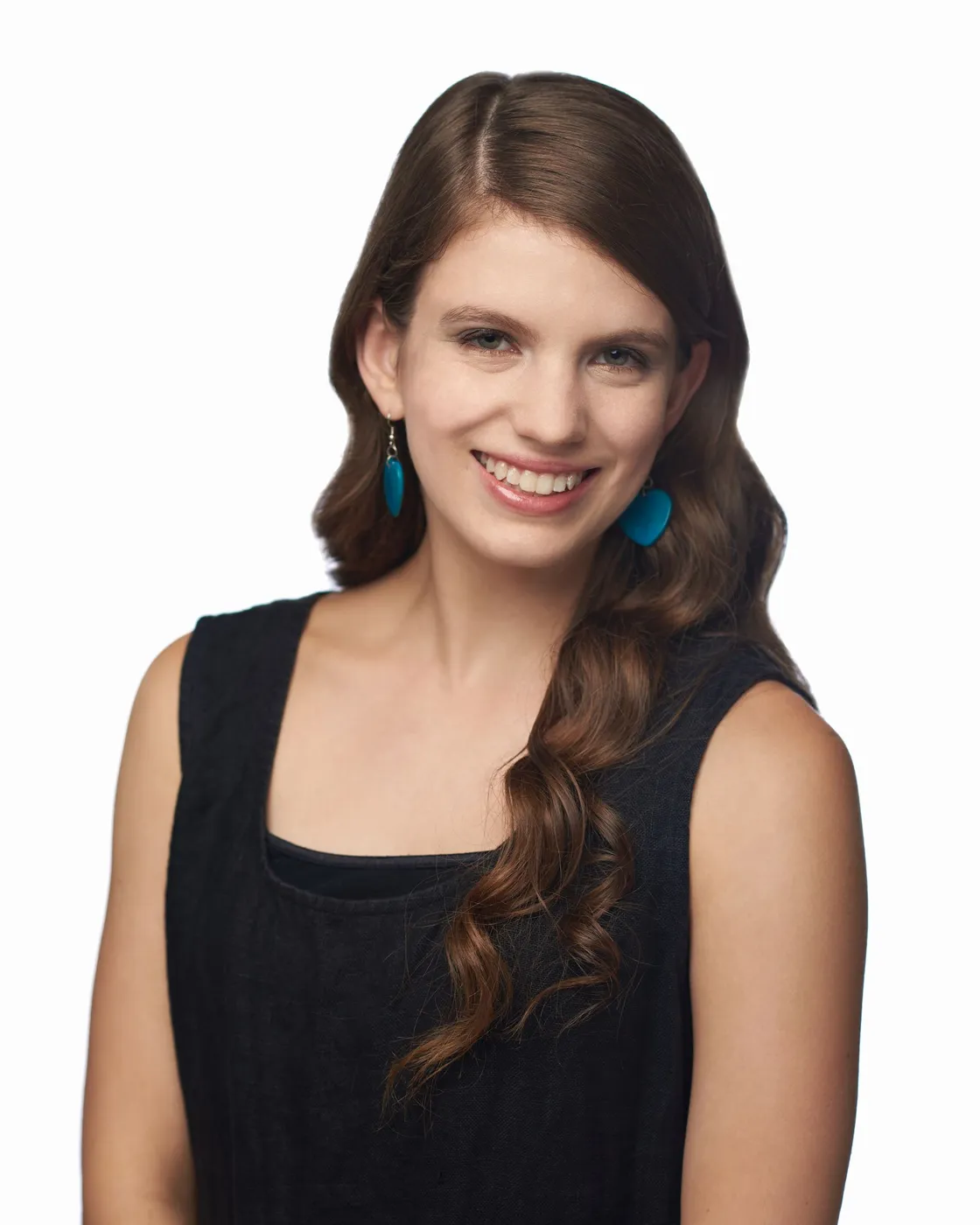 Woman with long brown hair smiling, wearing a black top and blue earrings against a white backdrop.