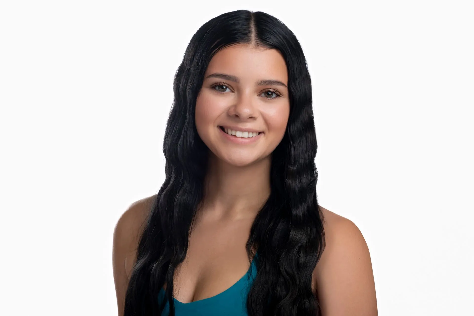 Woman with dark wavy hair smiles, wearing a teal top against a white background.