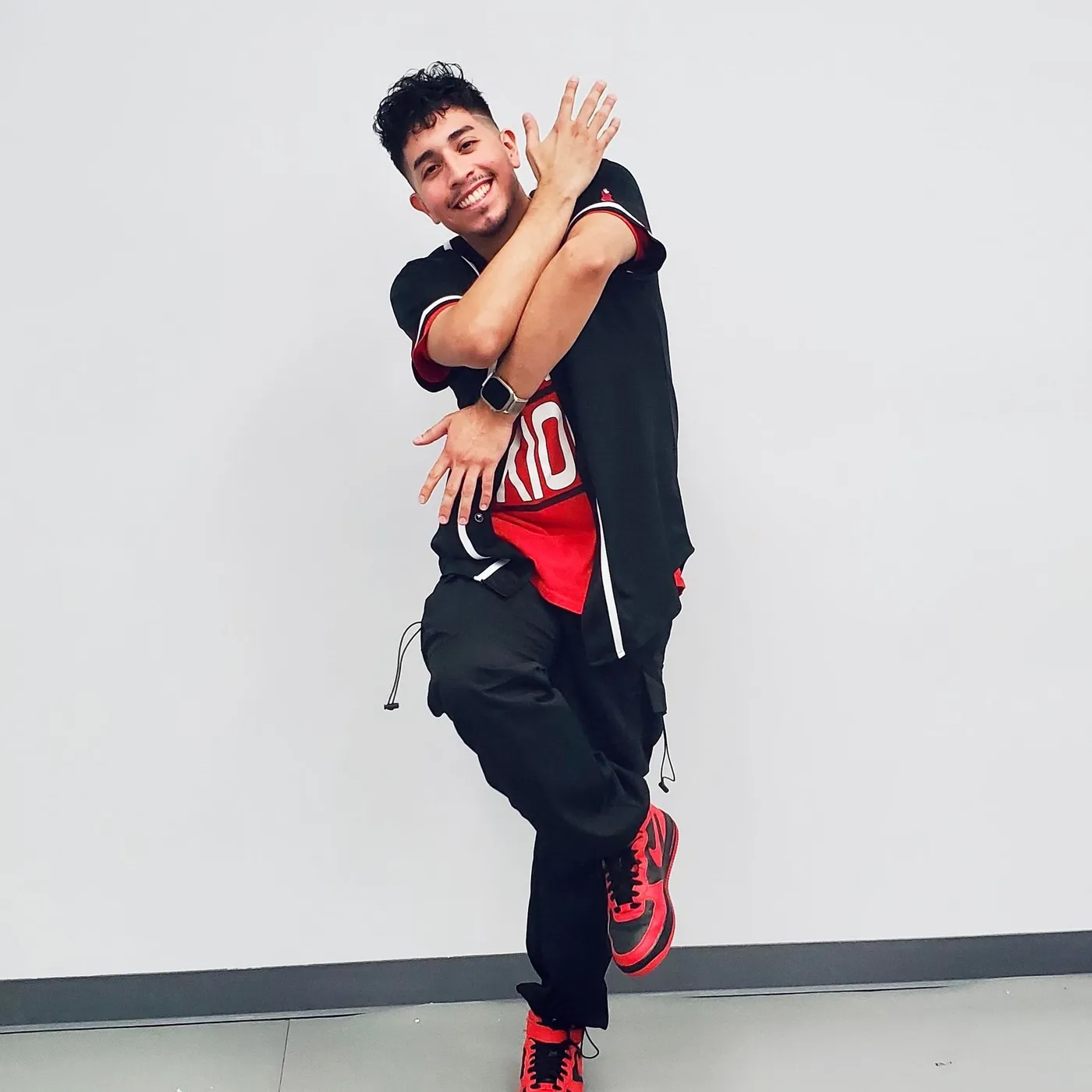 Man in athletic wear strikes a dance pose with arms crossed, red and black tones.