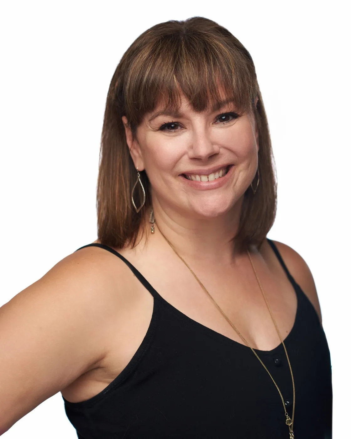 Woman with brown hair and bangs smiling, wearing a black tank top and gold necklace.