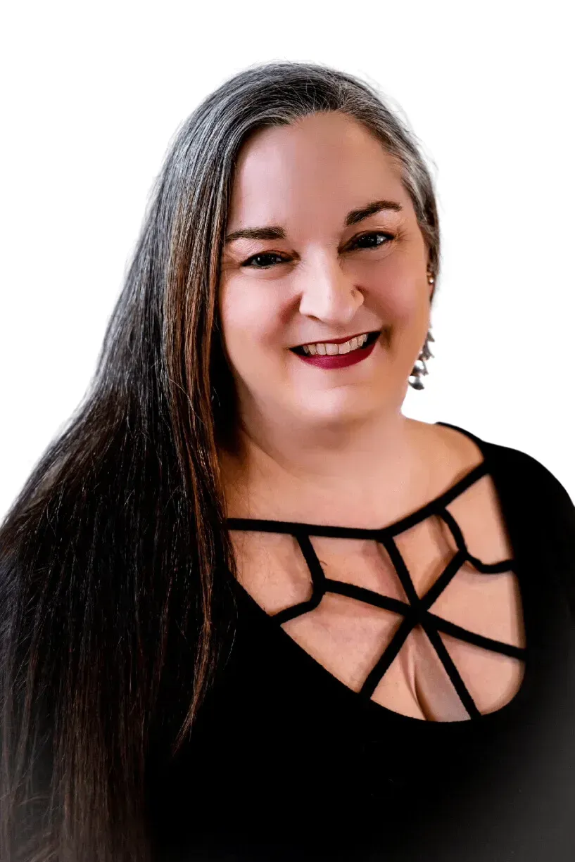 Woman with long, gray-streaked hair, smiling, wearing a black top with a geometric neckline.