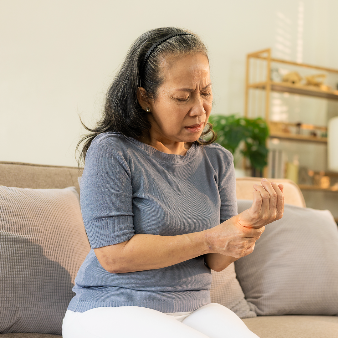 A woman is sitting on a couch holding her wrist in pain.
