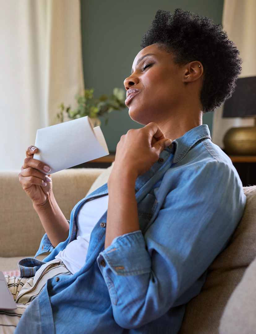 A woman is sitting on a couch reading a book and drinking coffee.