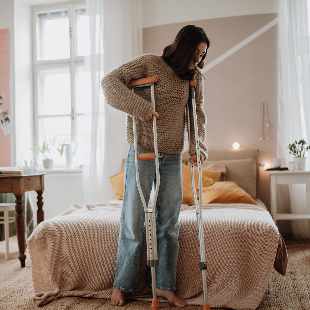 A woman with crutches is standing next to a bed.