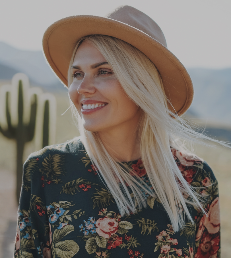 A woman wearing a hat and a floral dress is smiling.