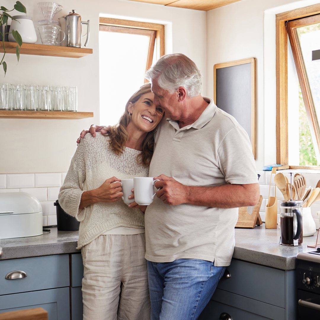 A man and a woman are standing in a kitchen holding cups of coffee.