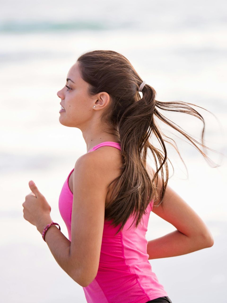 A woman in a pink tank top is running on the beach