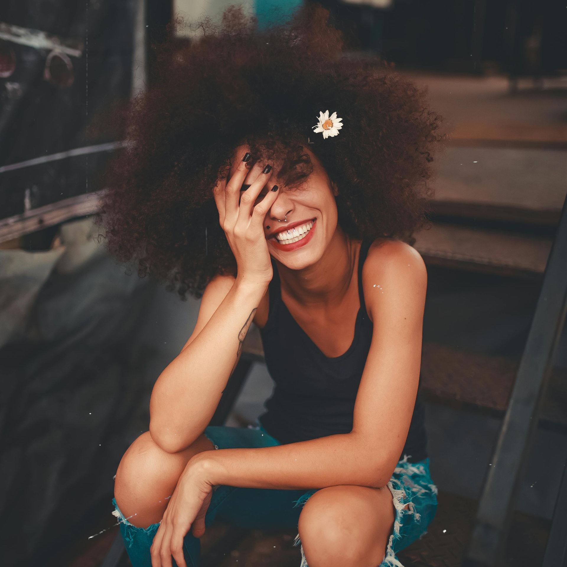 A woman with an afro is smiling and covering her face with her hand.