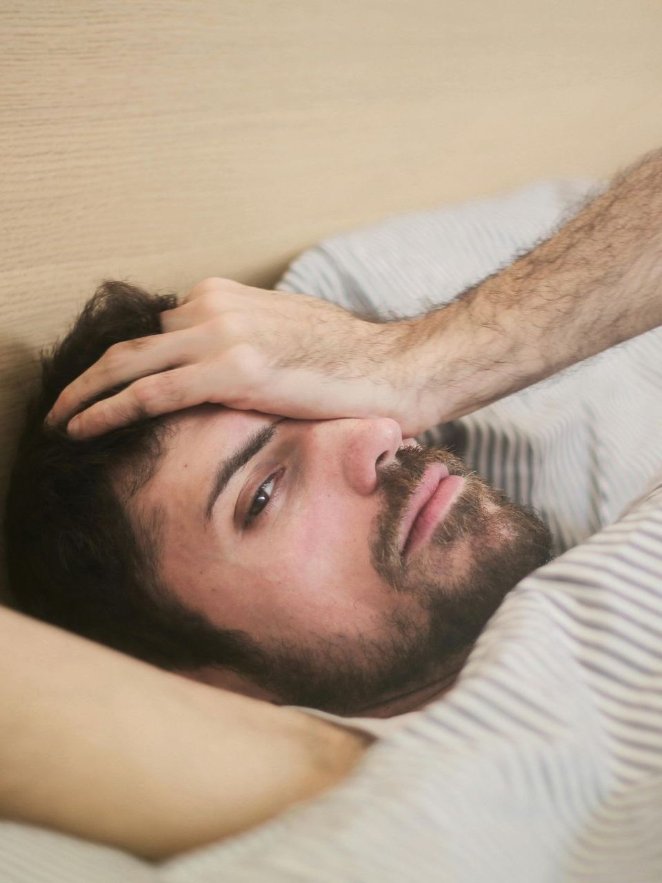 A man is laying in bed with his hand on his forehead.