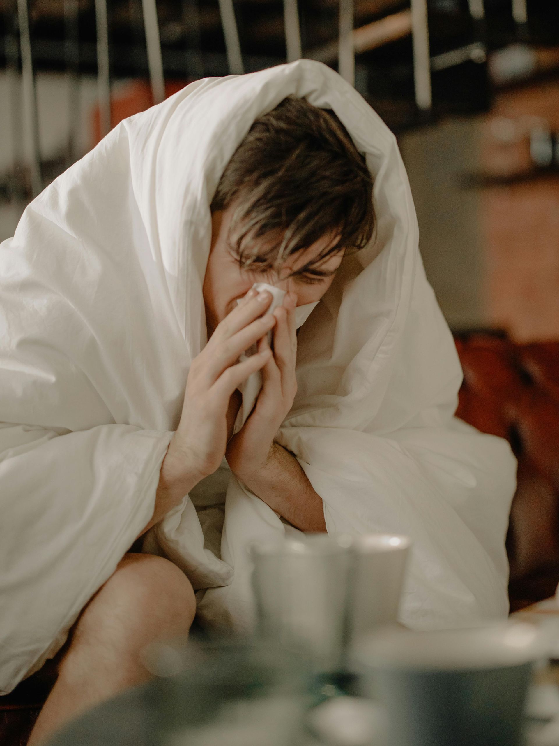 A man wrapped in a white blanket is blowing his nose.