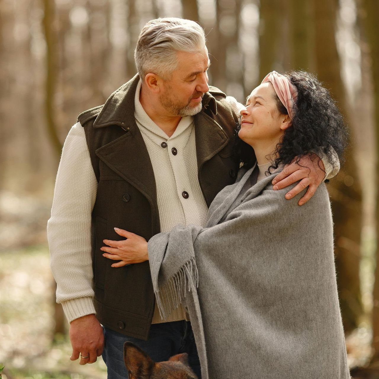 A man is hugging a woman wrapped in a blanket in the woods.