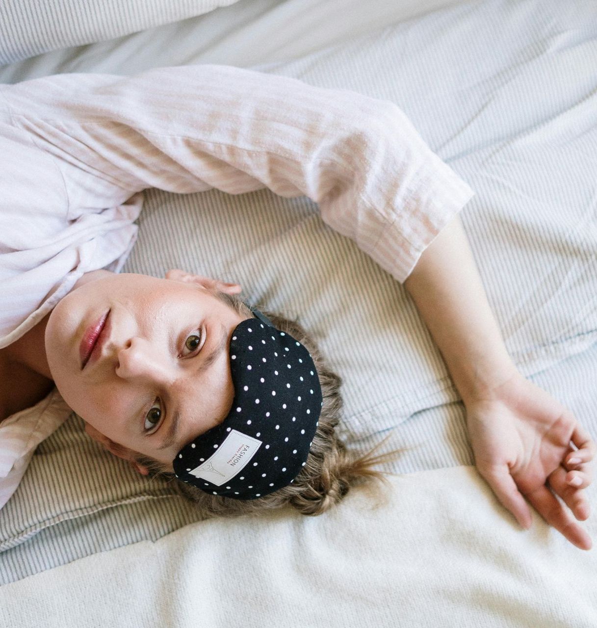 A woman wearing a sleep mask is laying on a bed