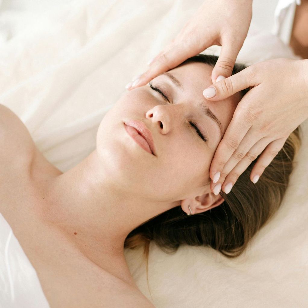 A woman is getting a facial massage with her eyes closed