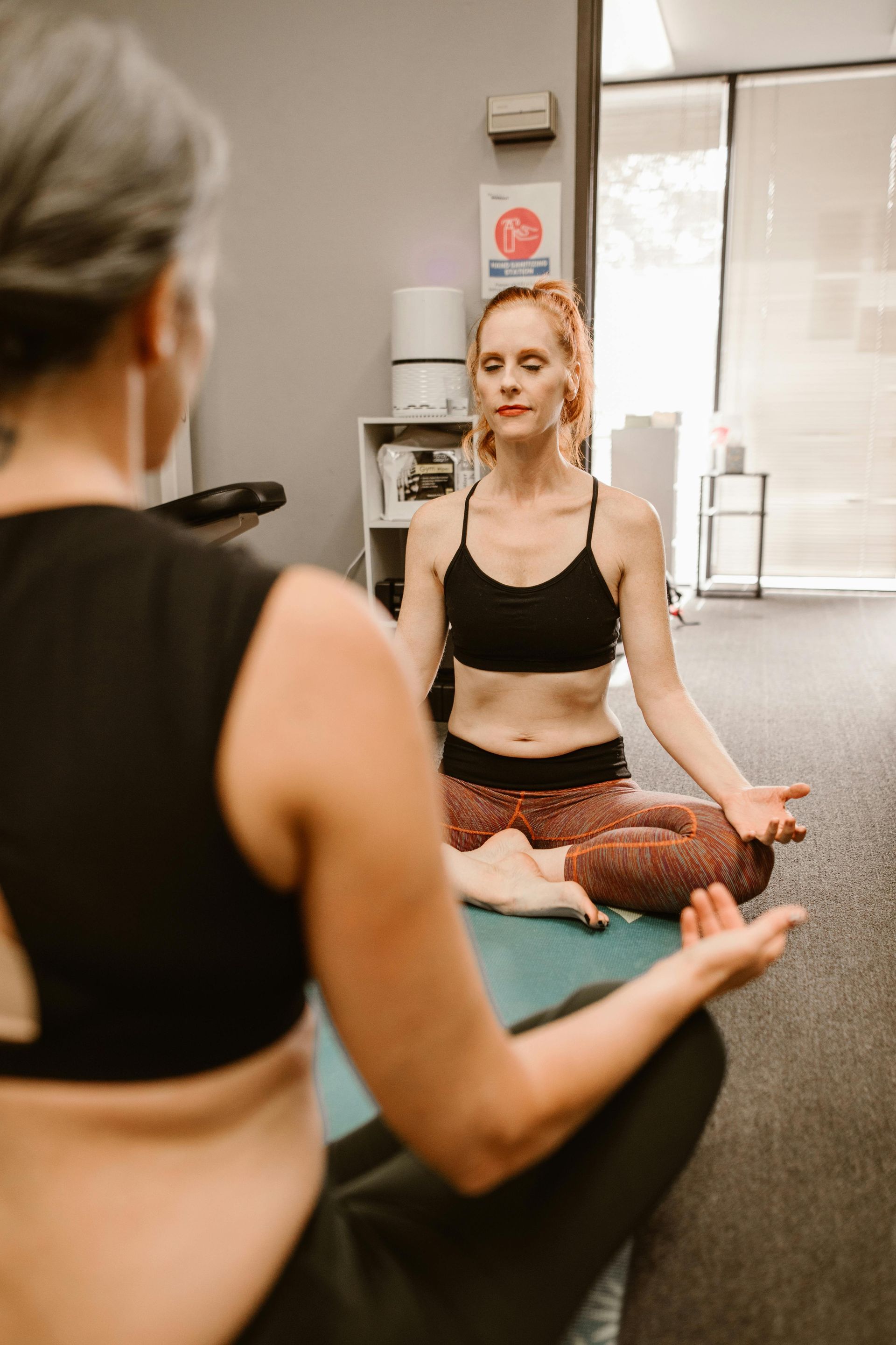 A woman is sitting on a yoga mat in front of a mirror.