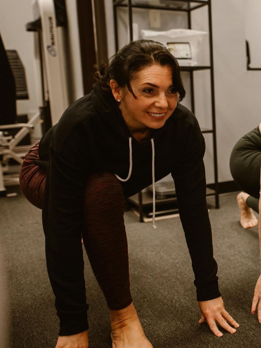 A woman is stretching her legs in a gym and smiling.