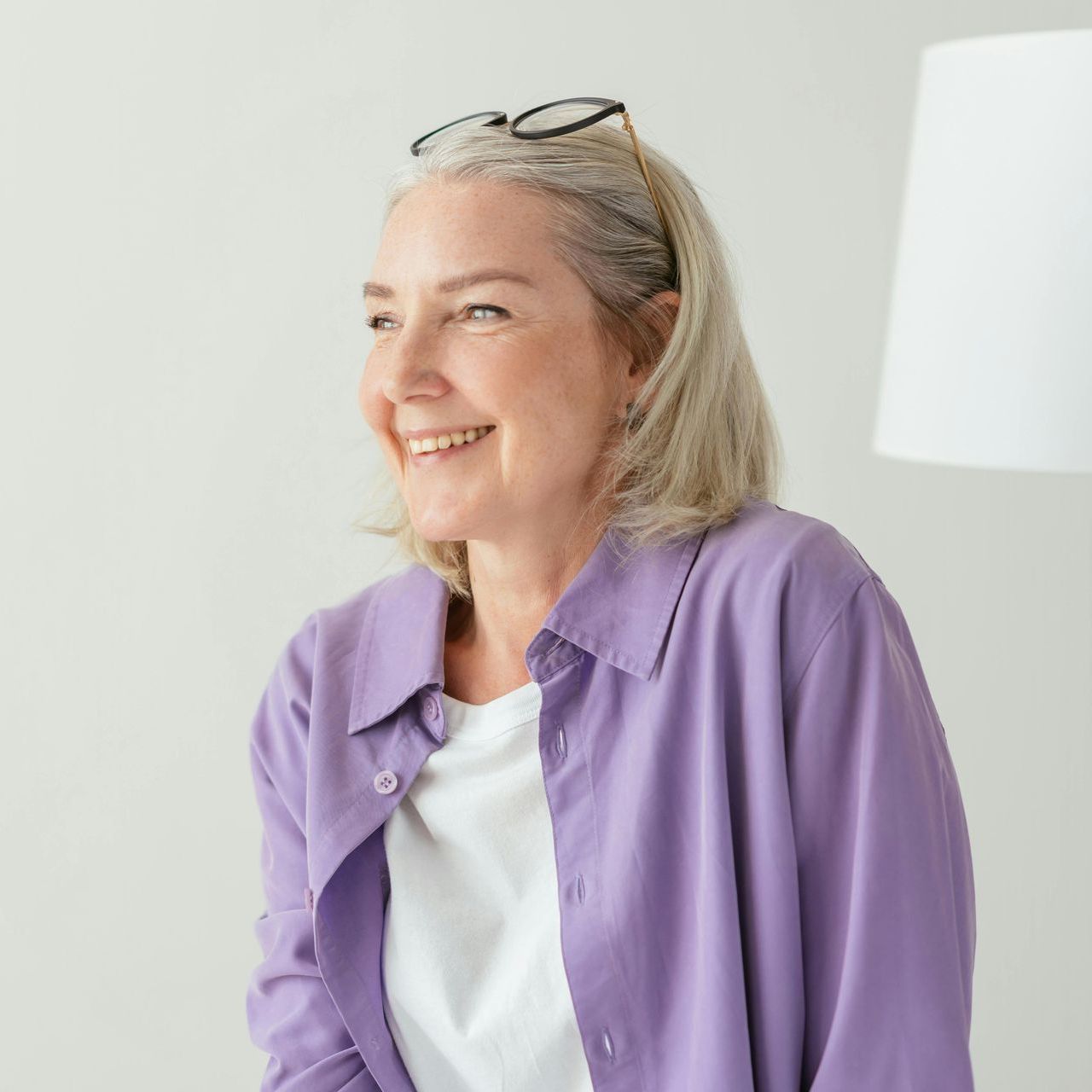 A woman wearing a purple shirt and sunglasses is smiling.