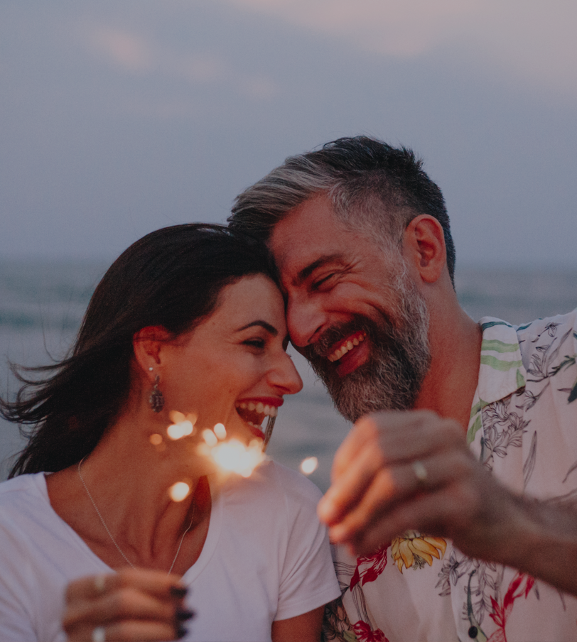 A man and a woman are holding sparklers and smiling at each other