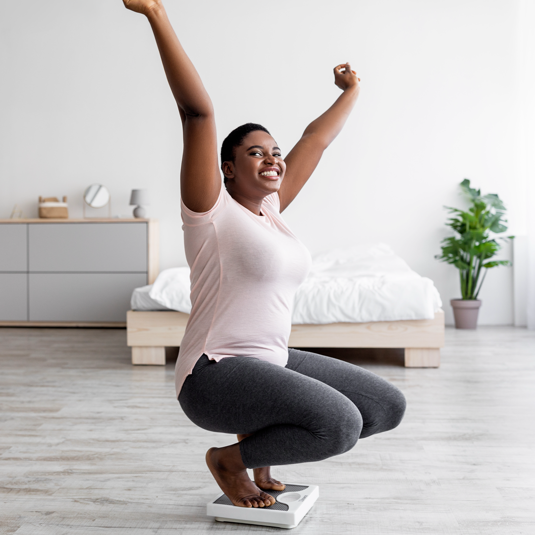 A woman is squatting on a scale with her arms in the air.