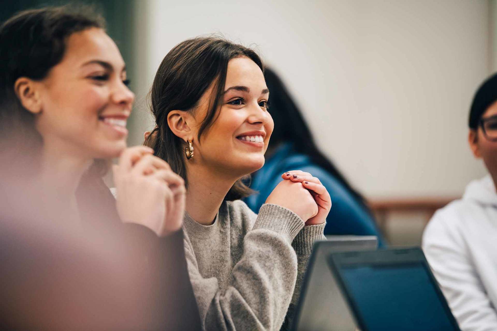 Smiling female students looking away while sitting in classroom
