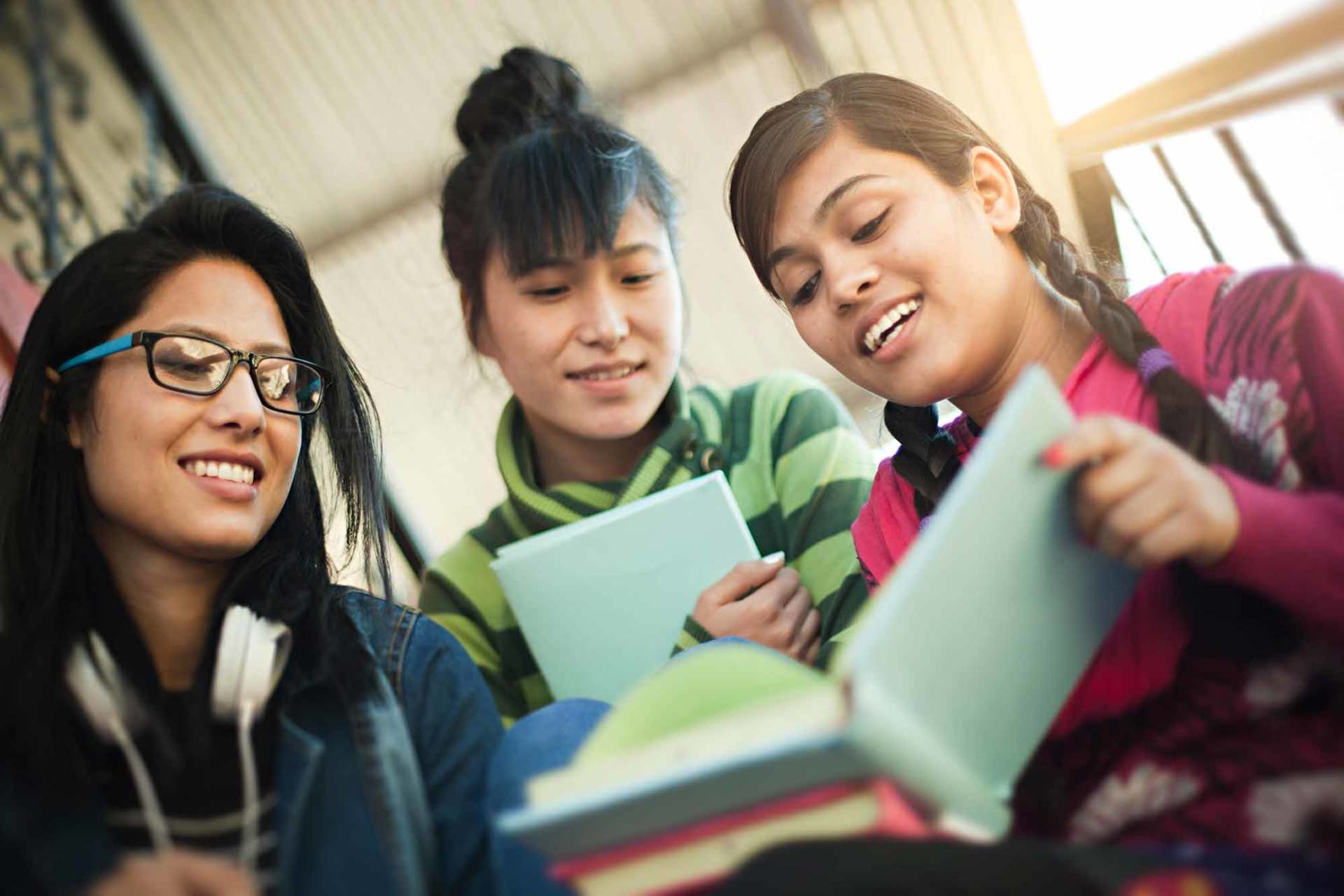 Outdoor low angle image of three late teen happy Asian girl students of different ethnicity studying together