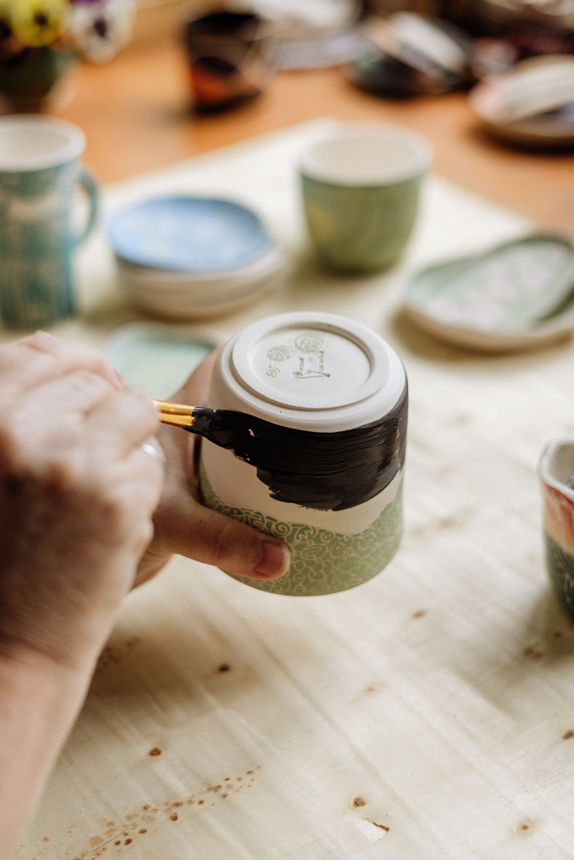 Image of a hand painting dark glaze onto a pot