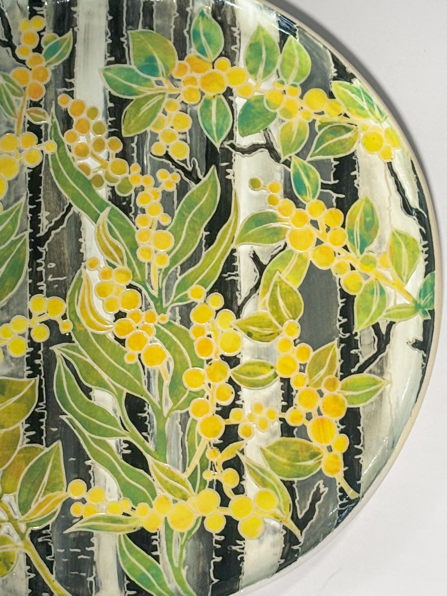 A platter covered in bright wattle flowers and a background with blues, oranges, reds, greens in all different patterns and textures. 