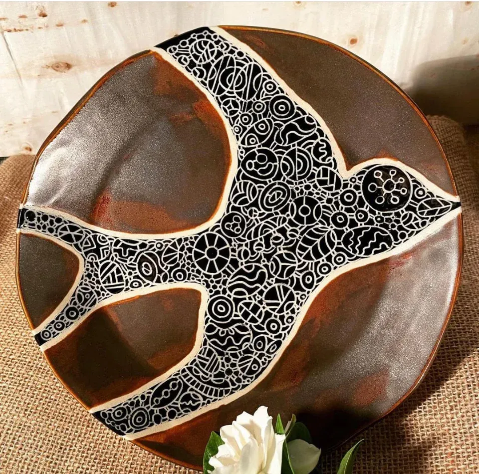 Ceramic plate with bird design, black and white detail over a brown background.