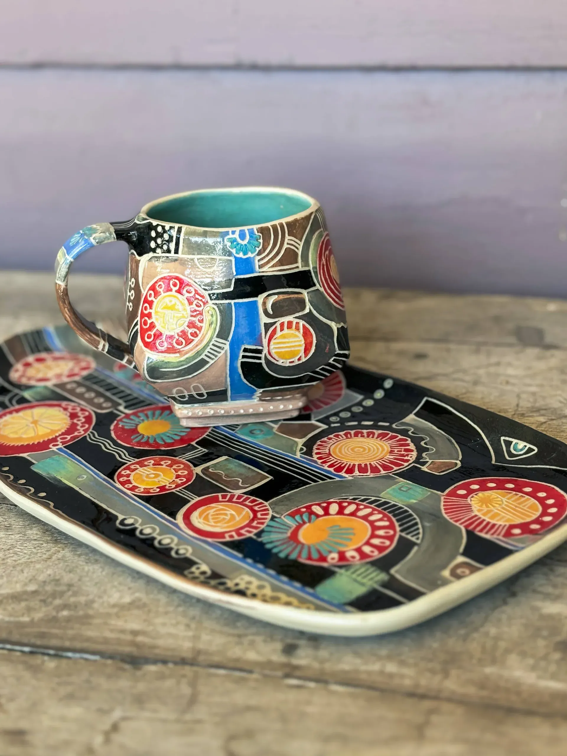 Ceramic mug and rectangular platter with colorful abstract designs on a wooden surface.