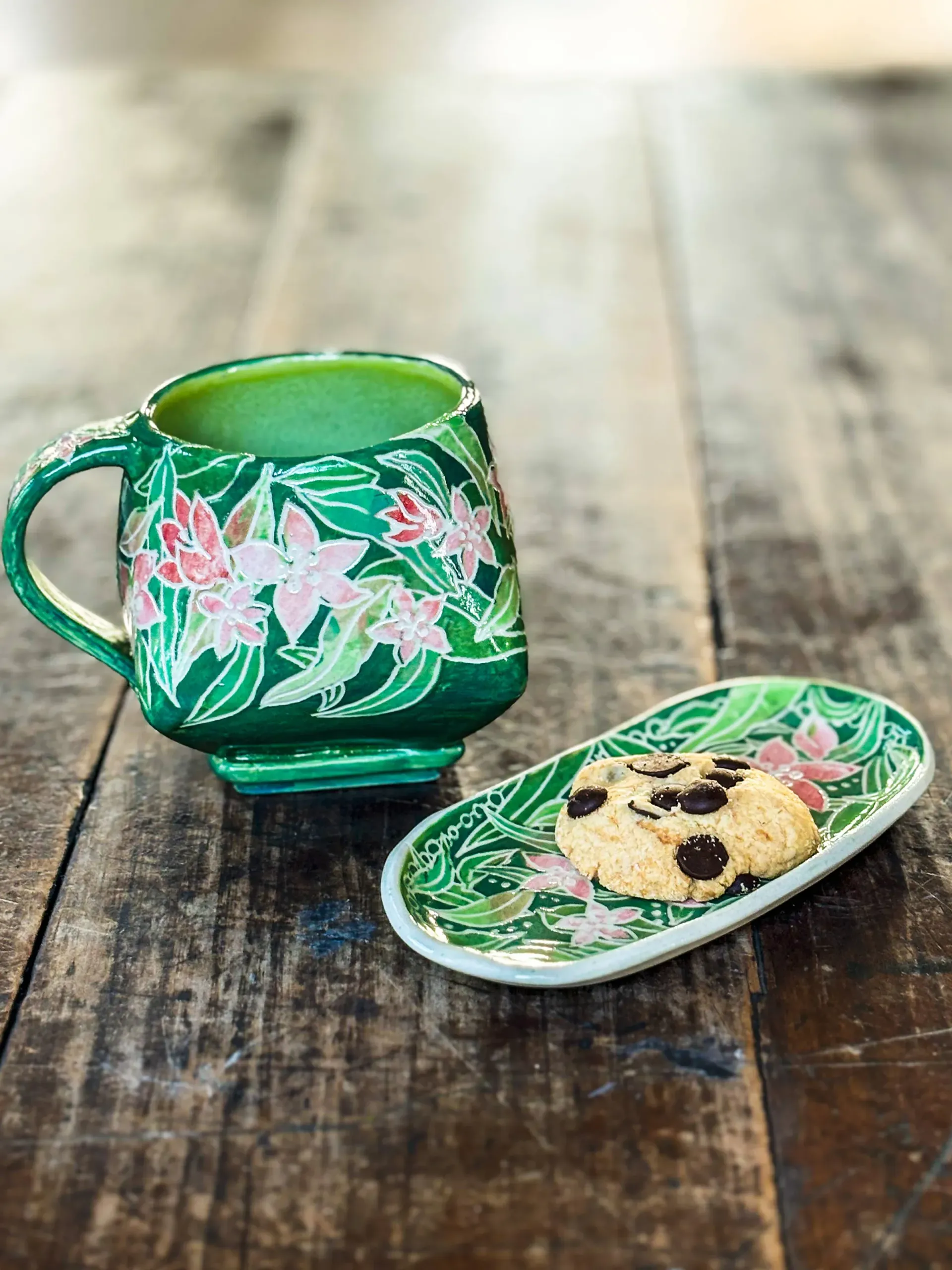 Green mug and matching plate with floral design, set on wooden table, cookies on the plate.
