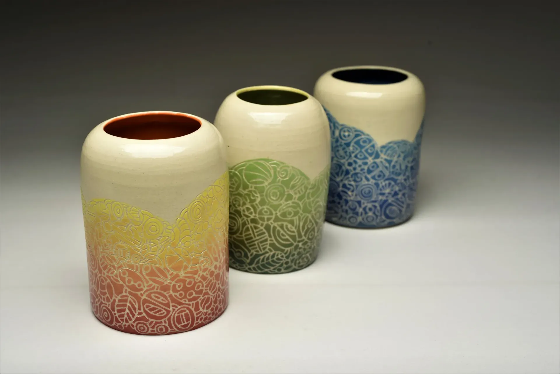 Three ceramic vases: yellow, green, and blue with patterned bases, white tops, and different colored interiors.