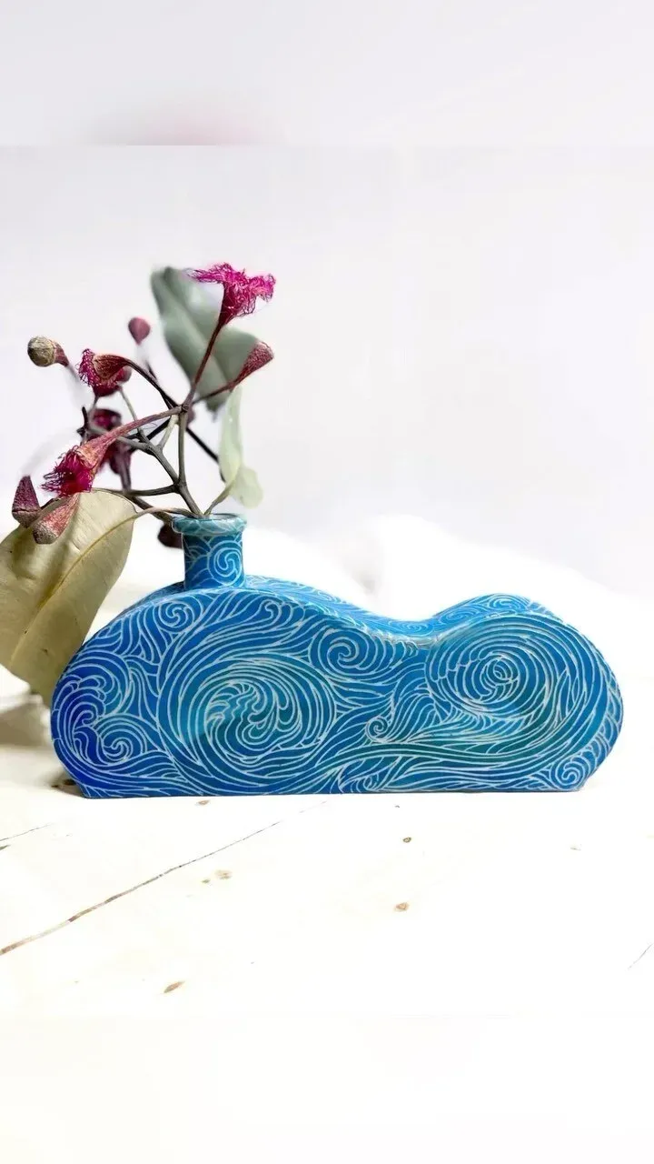 Blue, patterned vase holding pink flowers on a white wooden surface.