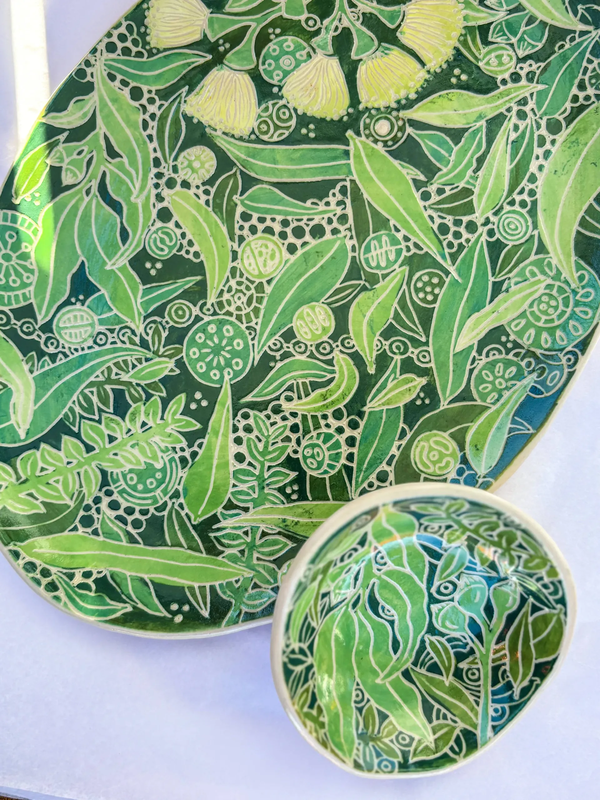 Oval and round ceramic dishes with green eucalyptus leaf pattern on white background.