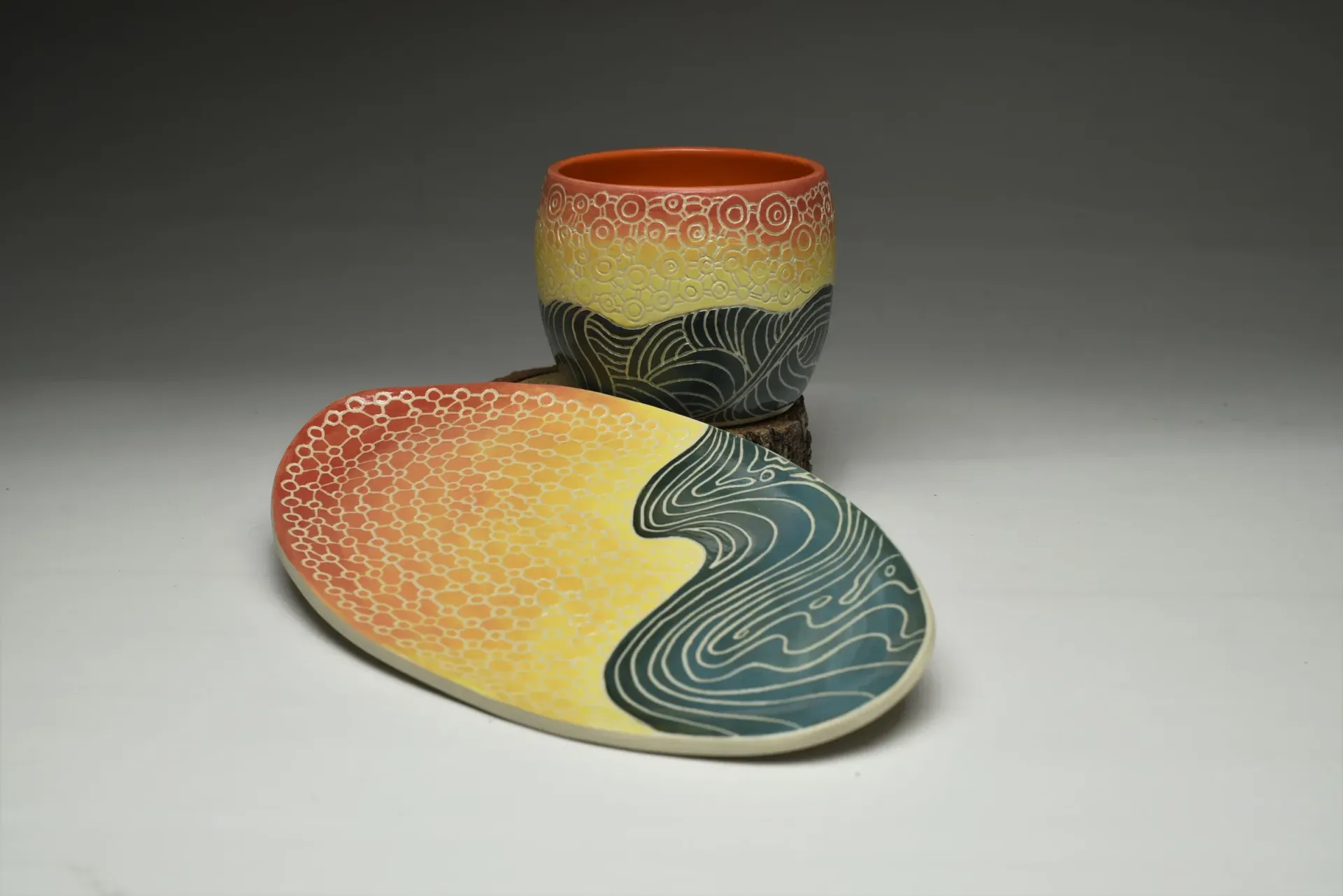 Ceramic cup and plate set, with abstract colorful design resembling landscape and water waves.
