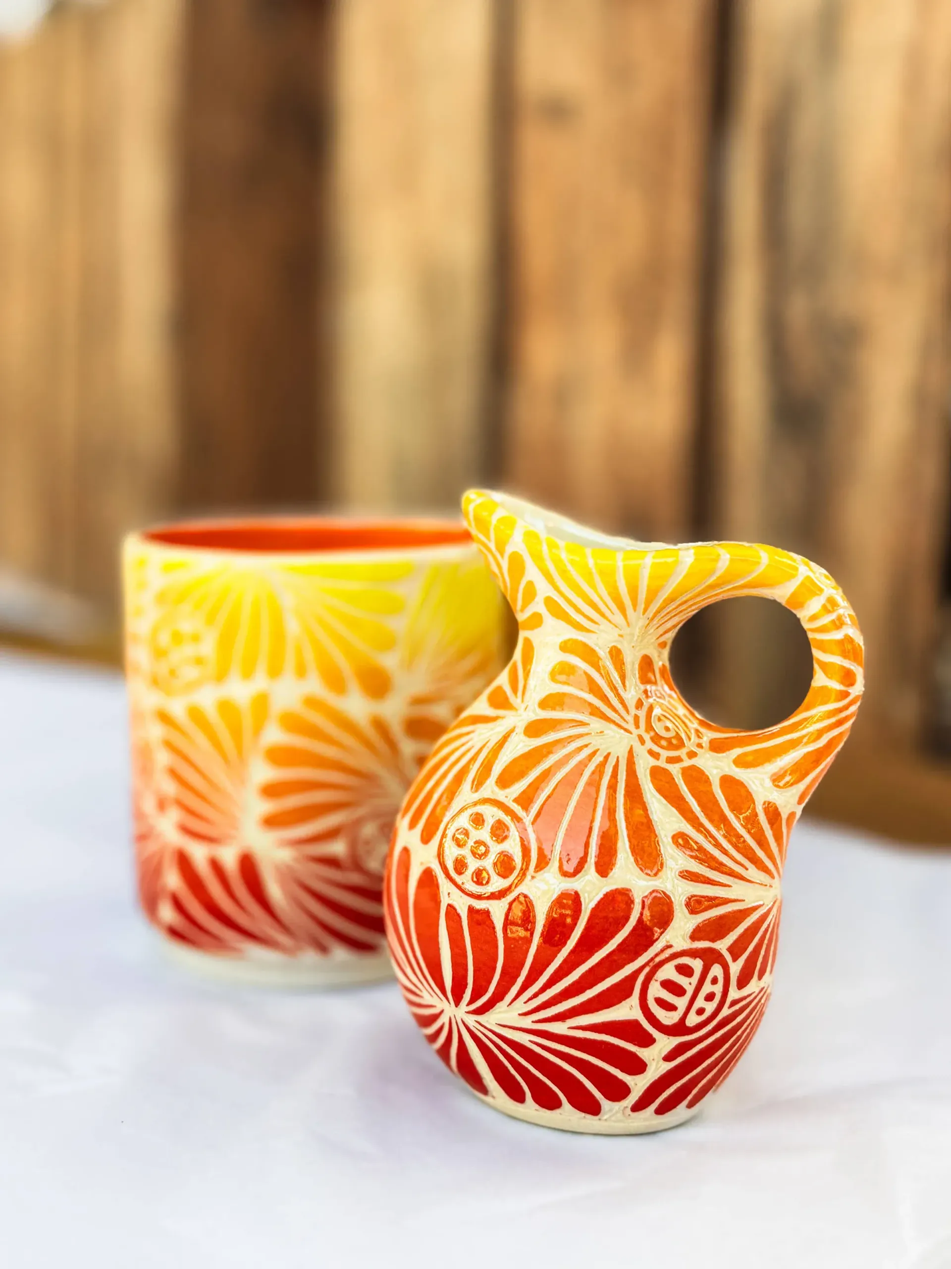 Small orange and yellow pitcher and cup with etched floral design.