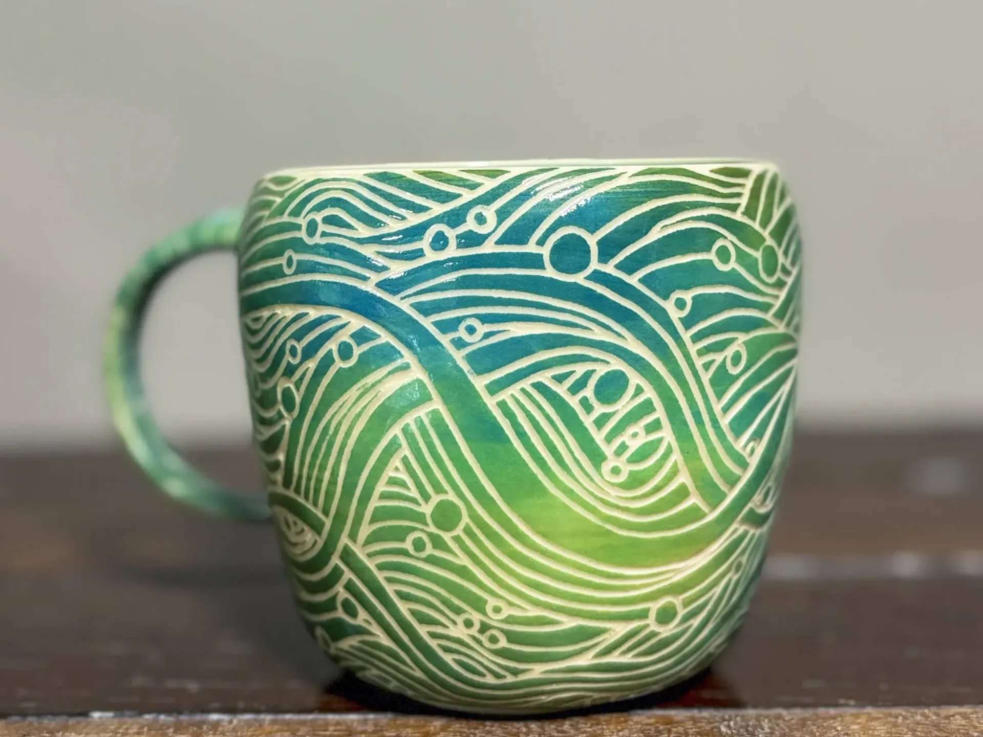 Ceramic mug with green to blue gradient. Carved wave-like design with little bubbles interspersed through the flowing lines.
