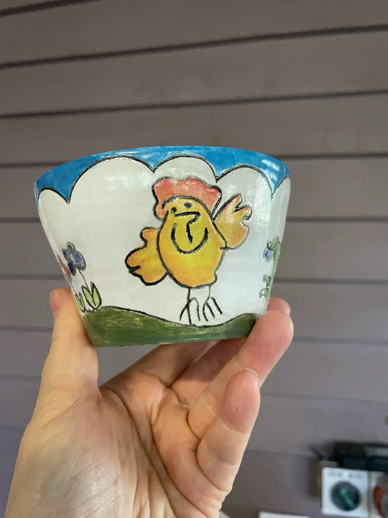 Hand holding a small, white bowl with a cartoon chicken and flowers; blue scalloped rim.