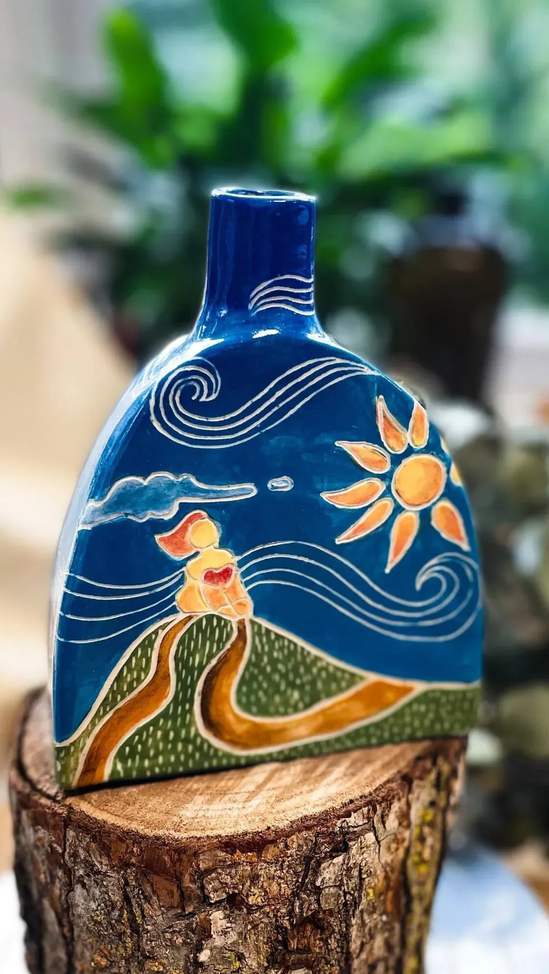 Blue ceramic vase with landscape: sun, hills, clouds, and figure.