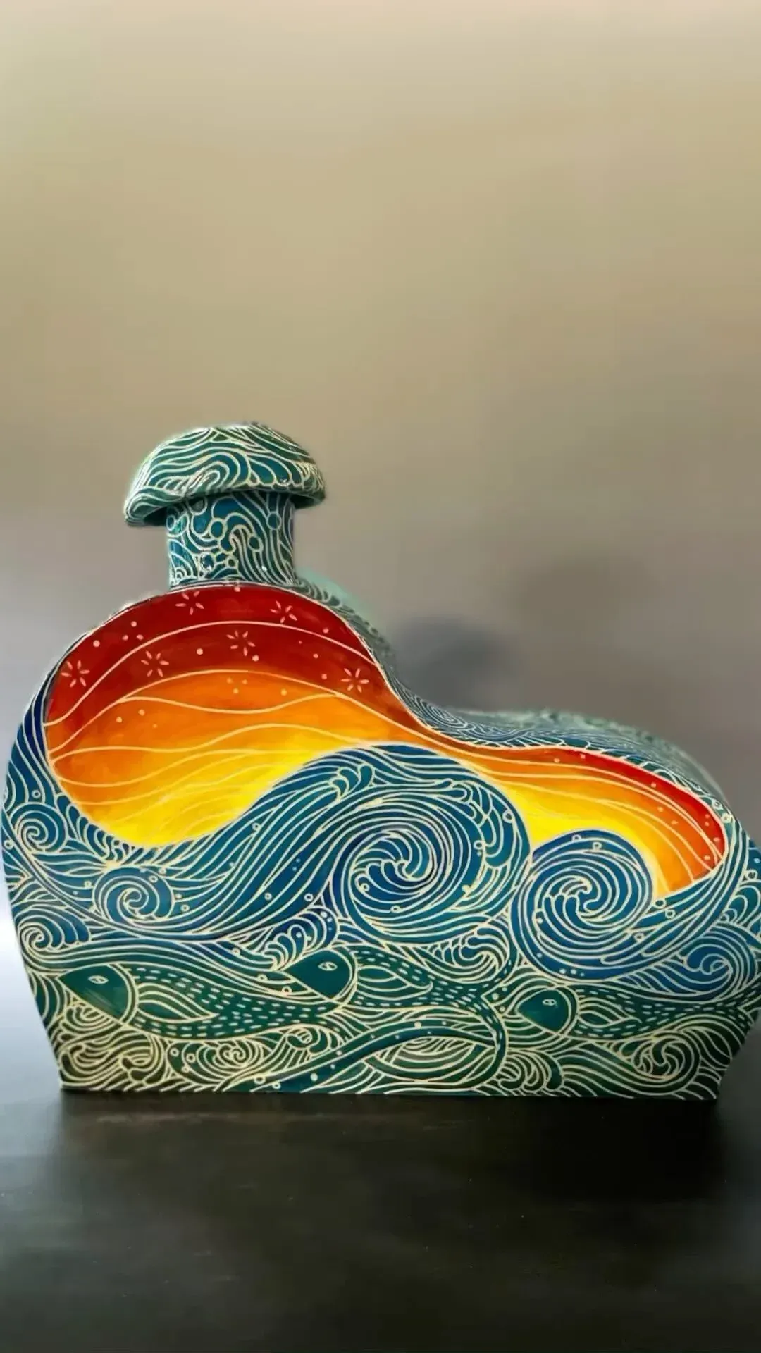 Blue and white wave-patterned art piece with a fiery sunset design; on a reflective surface.