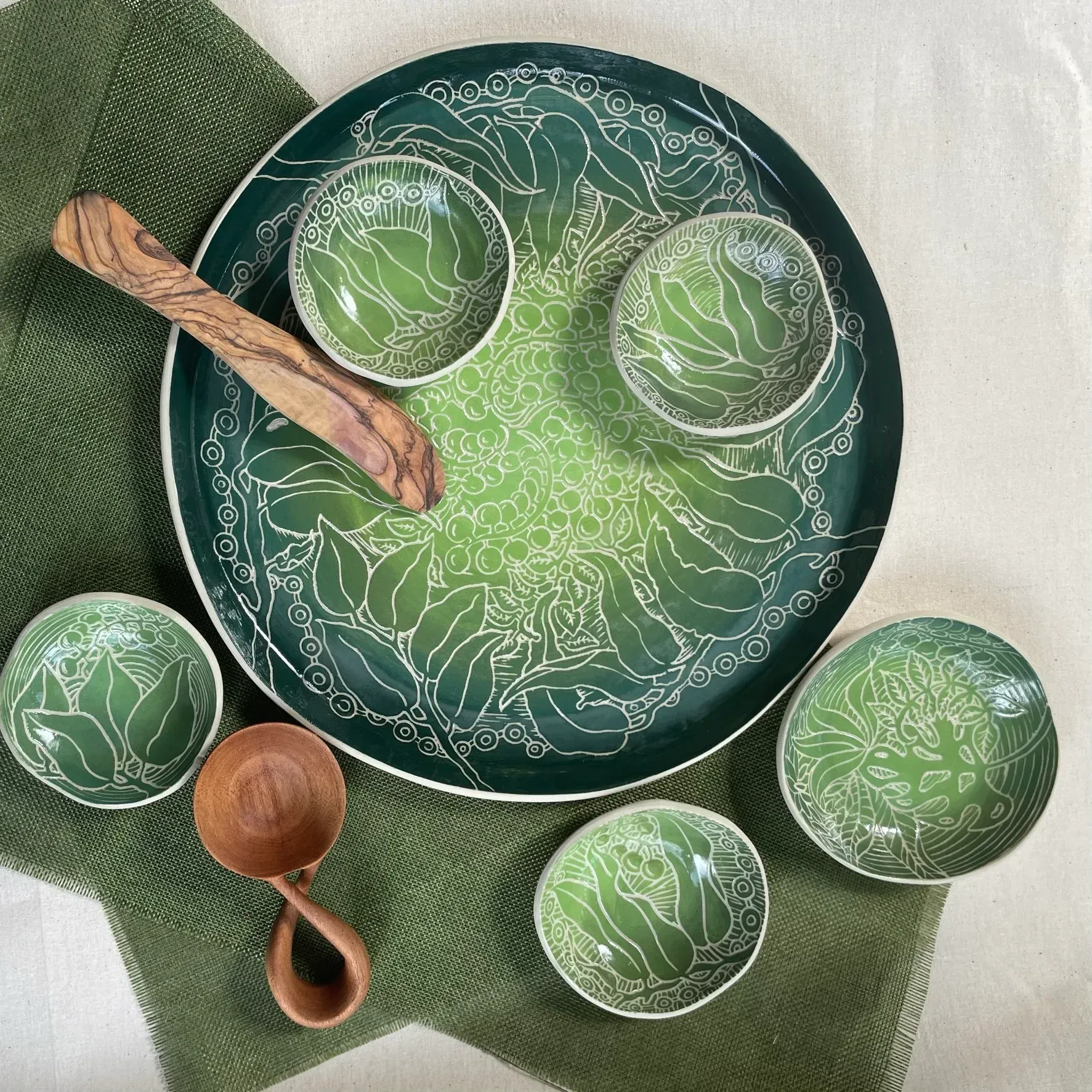 Green serving set: plate, bowls, and spoons on a green textile.
