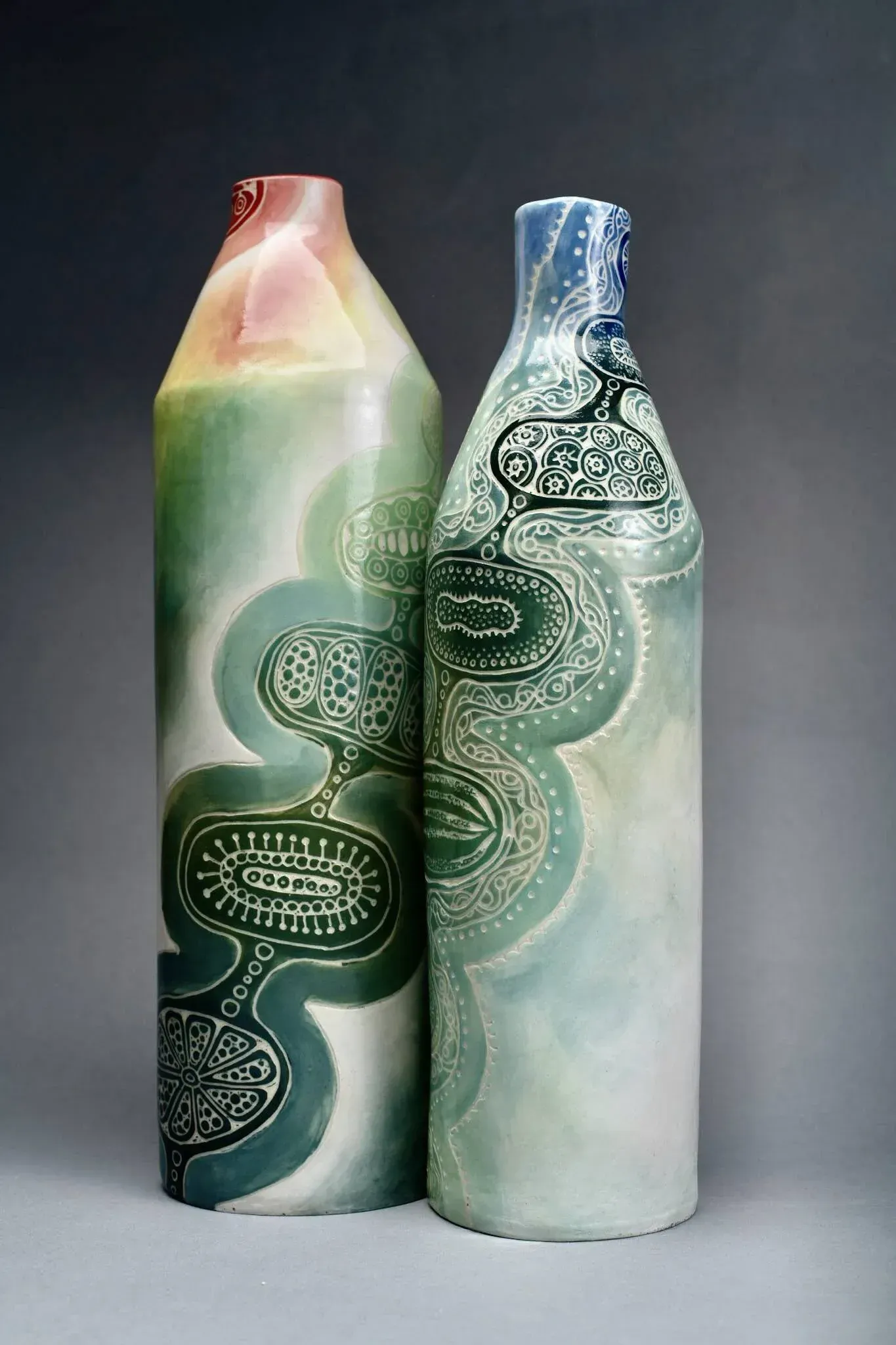 Two tall ceramic vases, one green and one blue, with swirling, etched designs.
