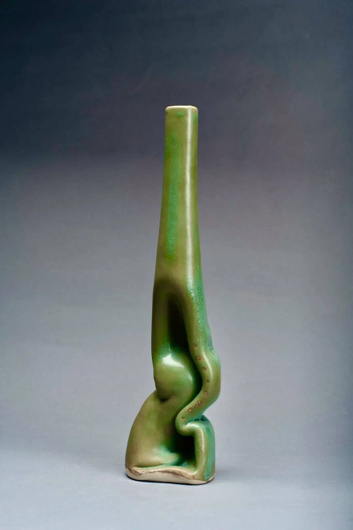 Green ceramic vase, tall and narrow, with an organic, folded shape.