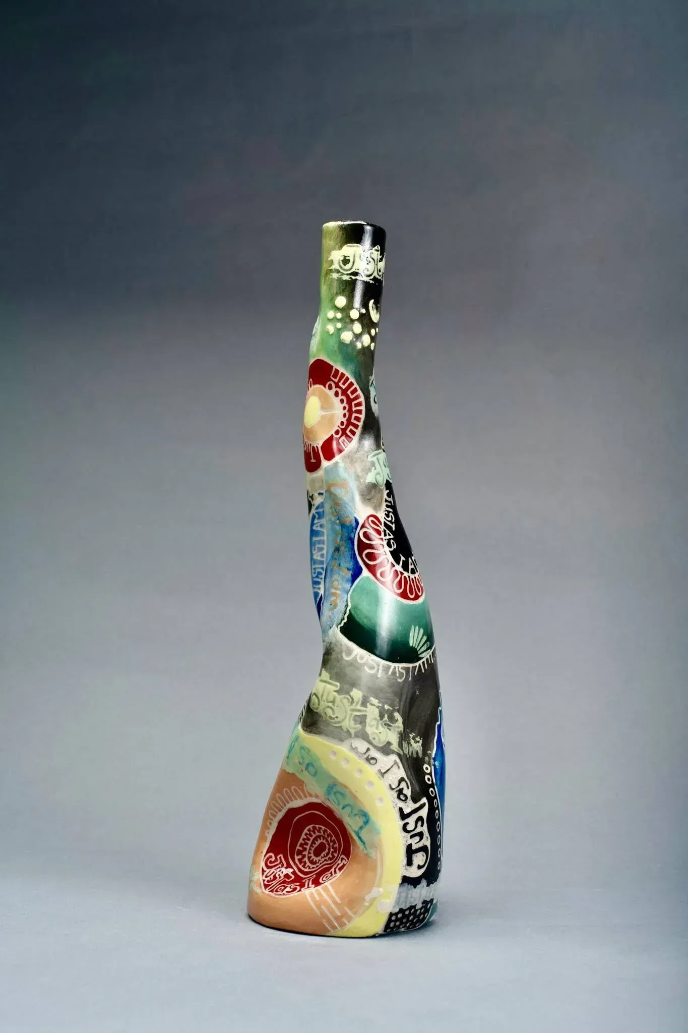 Colorful, tall, ceramic vase with patterned, irregular surface; against gray background.
