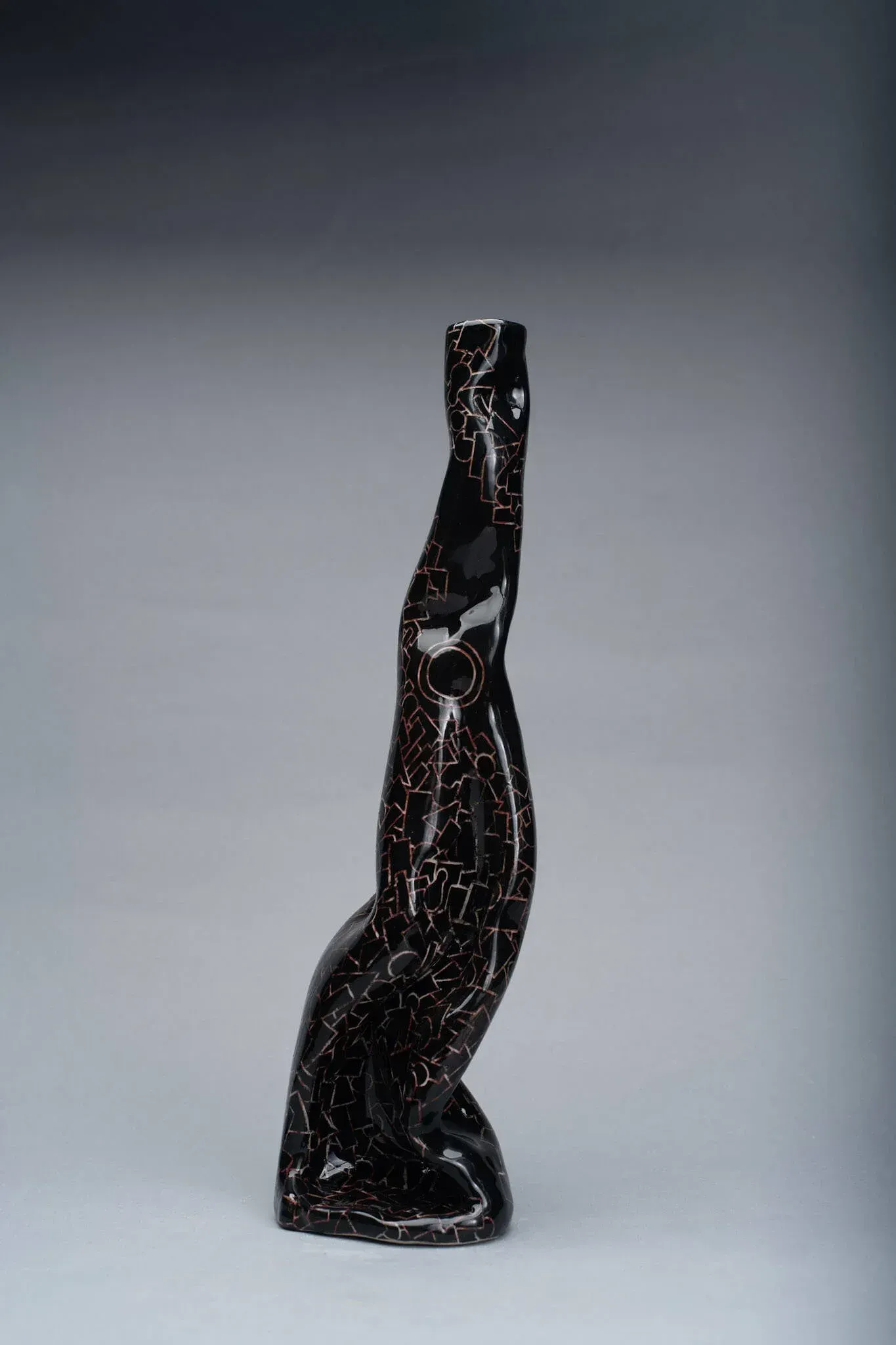 Black, glossy vase with flecks of gold, curving shape on a gray background.